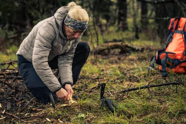 survivalist woman igniting a campfire in a forest.