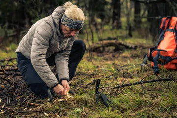 survivalist woman igniting a campfire in a forest.